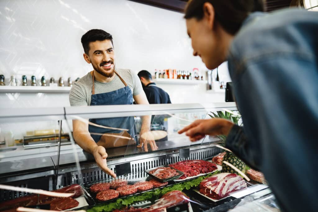 Butcher's shop seller helps to choose product to woman customer, close up