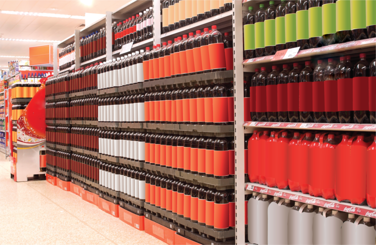 Store shelves filled with rows of large beverage bottles in various colours, neatly stacked on reusable plastic trays for efficient display and easy restocking, showcasing a well-organised retail presentation.