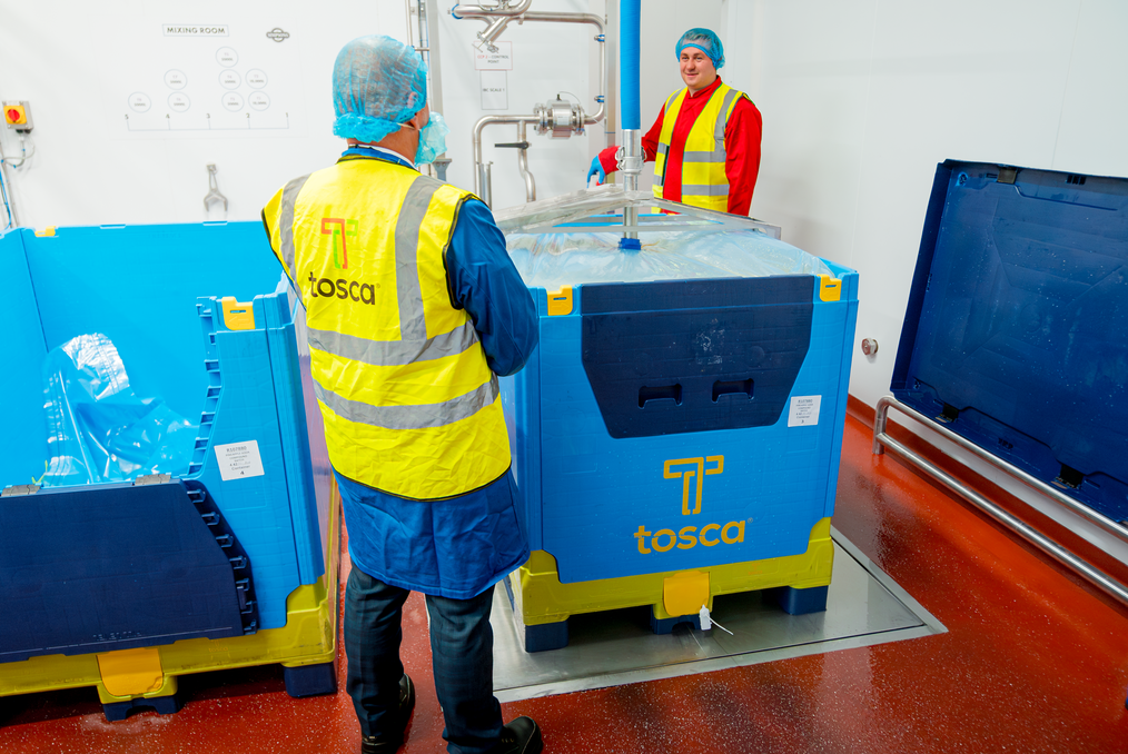 Two workers in a food processing facility handling a filled Tosca-branded reusable bulk beverage containers with a liquid liner, highlighting a hygienic and efficient solution for transporting liquid products.