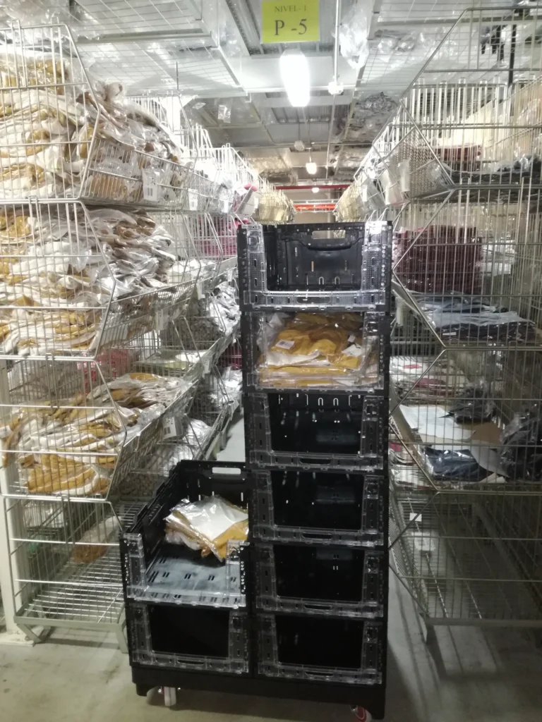 Products being restocked in crates with an open front, stacked on a portable pallet in a retail backroom. These general-use crates are easy to display as textile display racks.