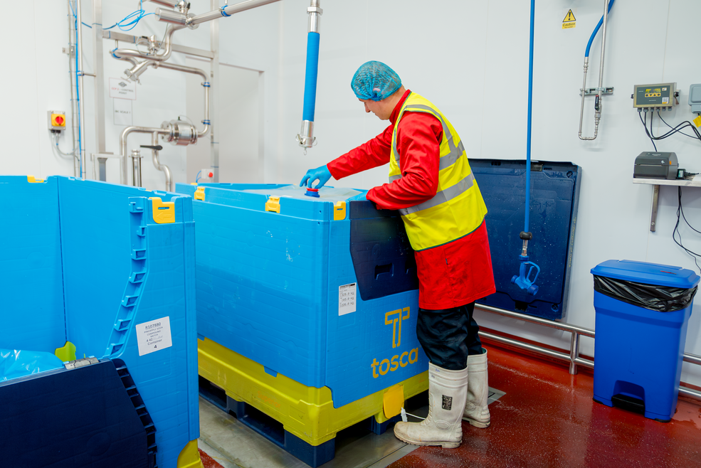 Worker standing beside a bulk container filled with liquid, prepared for hygienic and secure transport, showcasing a reliable solution for bulk liquid dairy handling in the supply chain