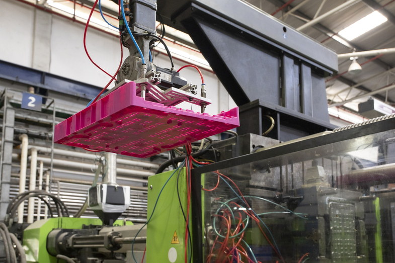 Close-up of automated machinery handling a vibrant pink reusable crate, showcasing advanced manufacturing processes in sustainable packaging solutions.