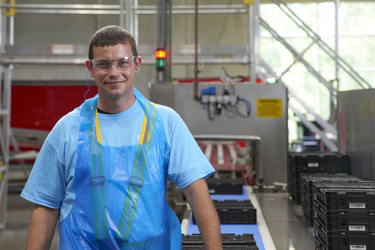 A Tosca service center worker wearing safety gear inspects reusable containers on a conveyor during the automated cleansing process.