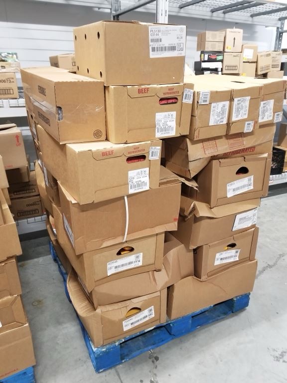 A wobbly stack of irregularly sized corrugated boxes sit on a wooden pallet inside of a distribution center.