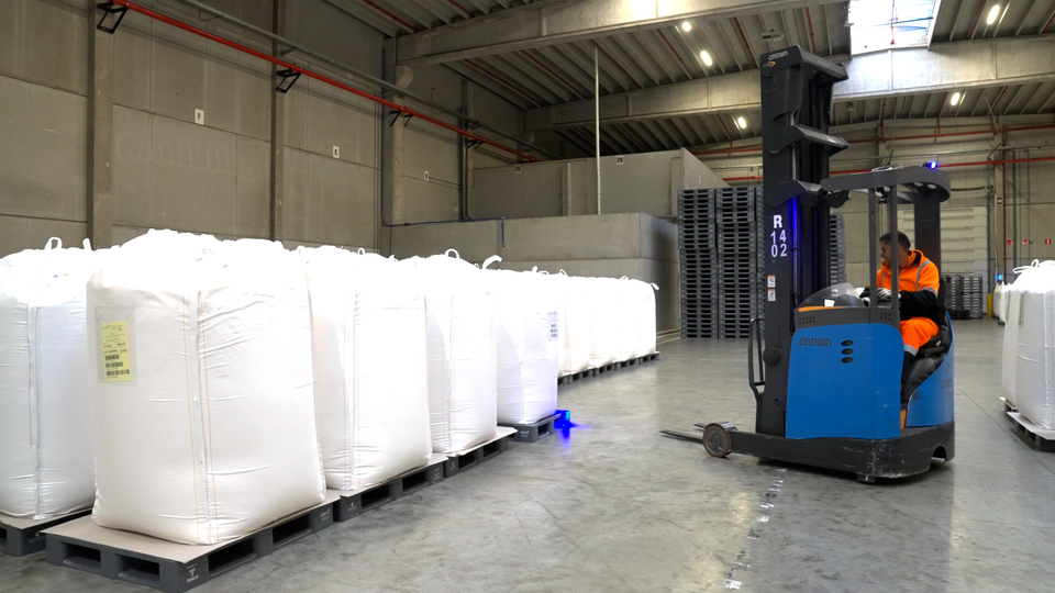 Bulk food ingredients in large bags placed on robust, durable reusable food grade plastic pallets, ready for secure transport in a warehouse, with a worker operating a forklift nearby.