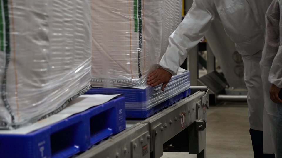 Close-up of a blue reusable plastic pallet supporting a heavy load of food packaging, highlighting its strength and durability for secure transport and storage
