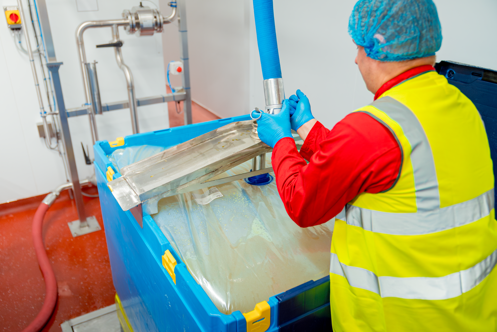 Worker handling a filling hose connected to blue reusable bulk beverage containers lined with a liquid liner, demonstrating a hygienic process for safely transferring liquid food products.