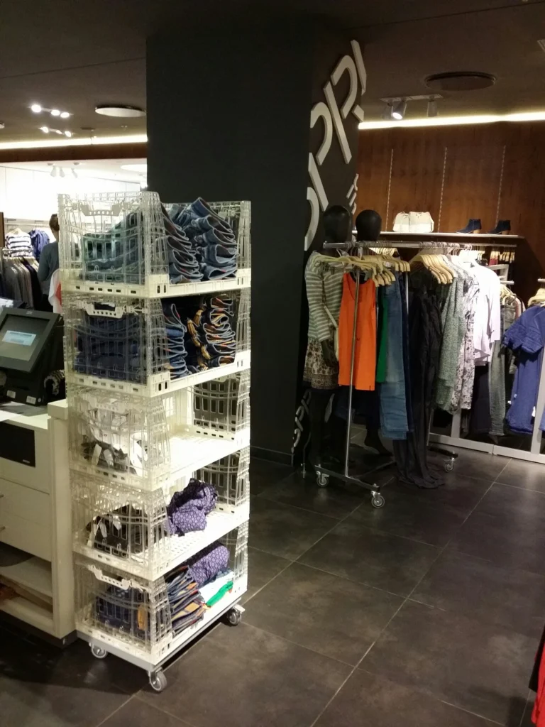 Tosca transparent plastic crates stacked on top of a mobile dolly for a point-of-sale display in a retail store, providing product visibility from all angles and a drop-down front for purchase and restocking convenience.