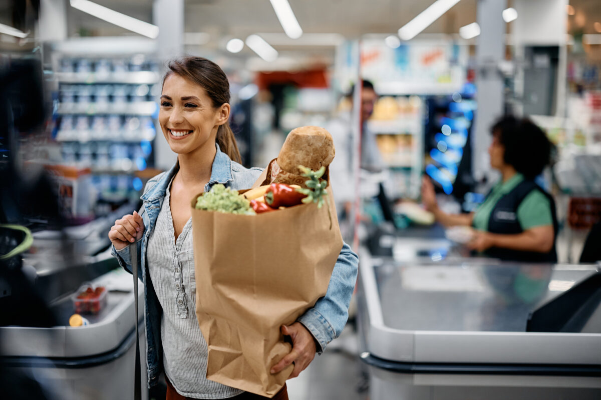 Young happy woman carrying paper bag with groceries after shopping in supermarket.