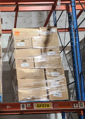 two pallets with corrigated boxes wrapped in shrink wrap sit racked inside of storage in a distribution center