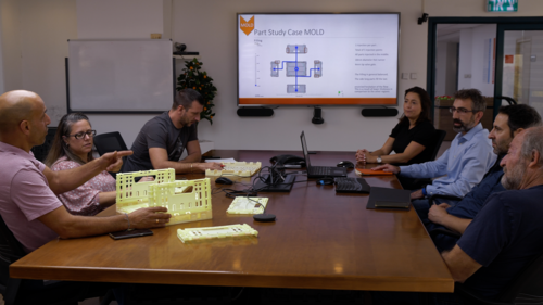 A team of Tosca R&D experts sit around a table in a conference room discussing a case study mold for customized market applications for reusable packaging assets.
