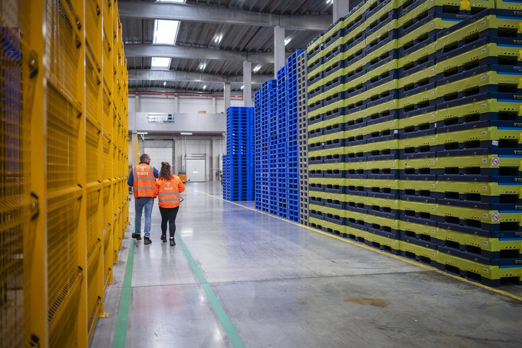 Workers in high-visibility vests walking through a Tosca facility, surrounded by neatly stacked reusable crates in vibrant yellow, blue, and green, highlighting efficient supply chain management