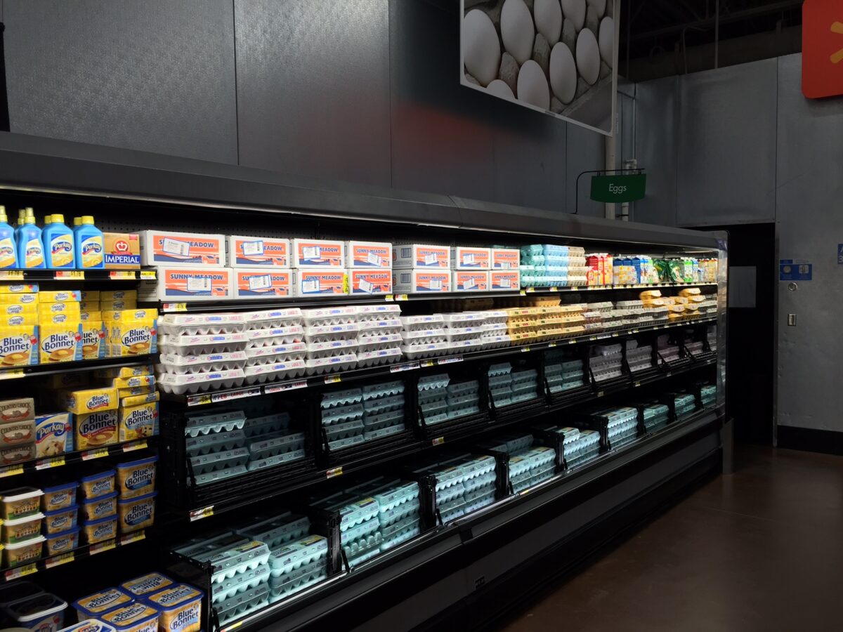 An organized grocery store egg section features Tosca reusable egg crates with a dropdown opening for easy access and restocking.