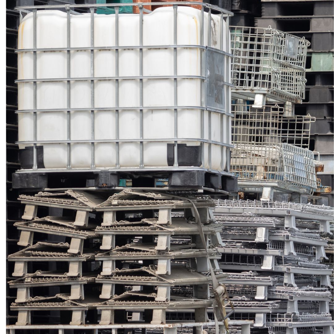 A caged intermediate bulk container sits on an unstable stack of pallets, demonstrating the drawbacks of rigid containers that lack the ability to fold and stack efficiently.