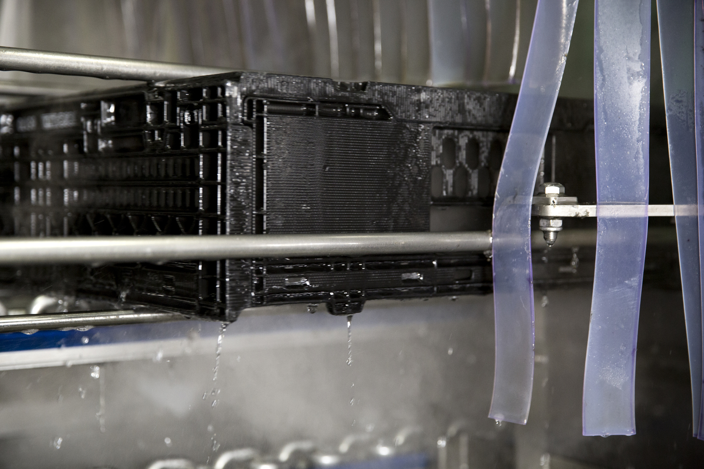 A freshly cleaned black plastic crate exiting an automated washer. Tosca ensures high food safety and quality assurance for optimal sanitation.